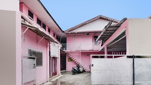 A pink building with a staircase leading to a second floor, a motorcycle parked in front, and a gated entrance. - Hotel O Raja Homestay Syariah (Pekanbaru)