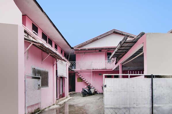 Un bâtiment rose avec un escalier menant à un deuxième étage, une moto garée devant et une entrée fermée par un portail.