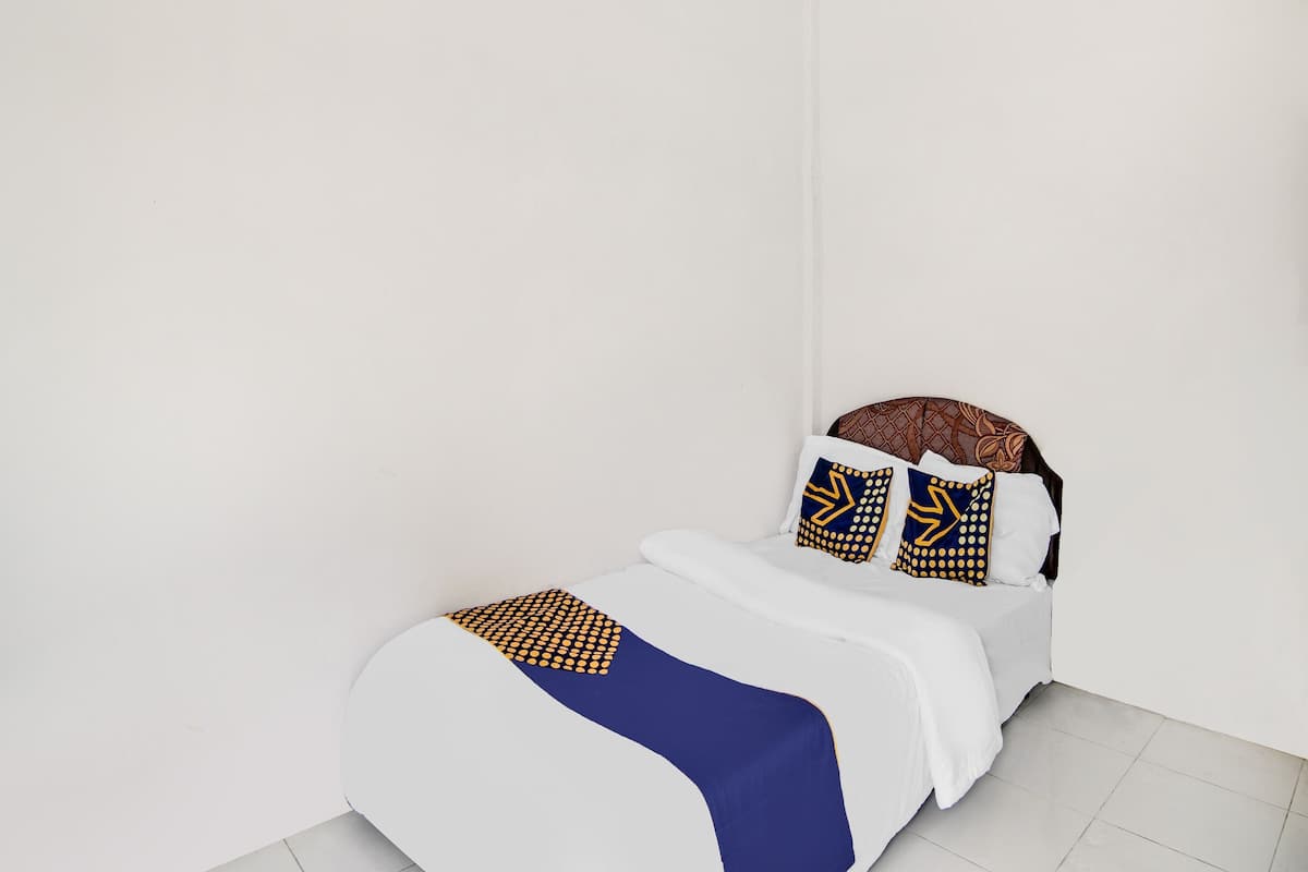 A single bed with a white and blue bedspread, two patterned pillows, and a brown headboard.