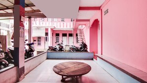 A courtyard with a wooden table, pink walls, and parked motorcycles. - Hotel O Raja Homestay Syariah (Pekanbaru)