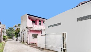 Une rue étroite avec un bâtiment rose, un mur blanc couvert de graffitis et un portail en métal.