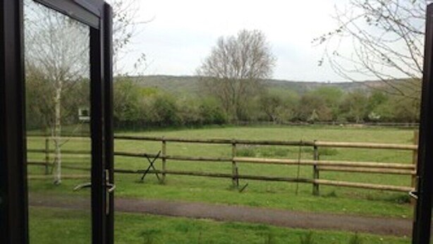 A view through a glass door of a grassy field with a wooden fence and a path.