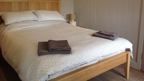 A neatly made bed with a wooden headboard, a bedside lamp, and folded towels on the bed.