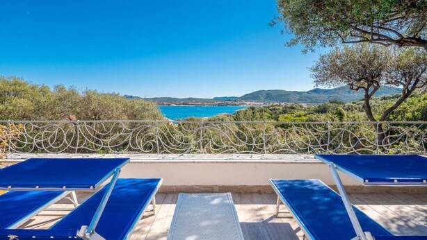 A terrace with blue sun loungers, a small table, and a view of the sea and hills. - Bellavista Paradise 2 (Marinella)