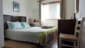 Een slaapkamer met een bed, een stoel, een nachtkastje en een raam.
