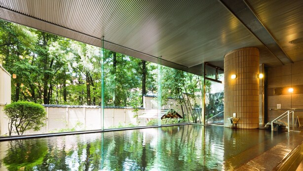 Una piscina interior moderna con paredes de vidrio transparente, suelo de baldosas y un pilar de madera.