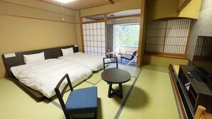 Una habitación japonesa tradicional con suelo de tatami, una cama con ropa de cama blanca, una silla azul, una mesita y un televisor.