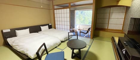 A traditional Japanese room with tatami flooring, a bed with white bedding, a blue chair, a small table, and a TV.