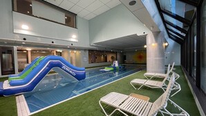 Una piscina interior con tobogán, césped artificial y sillas de descanso.