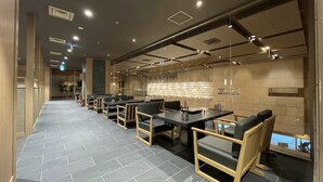 Un restaurante moderno con una barra alargada, sillas negras y suelo de baldosas.