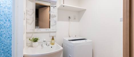 A bathroom with a white sink, a mirror, a potted plant, and a white washing machine.