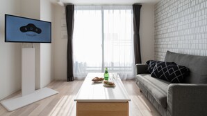 Een moderne woonkamer met een flatscreen televisie, een bank, een salontafel en een groot raam met gordijnen.