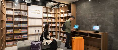 A hotel lobby with a seating area, a self-service kiosk, and a large bookshelf filled with books.