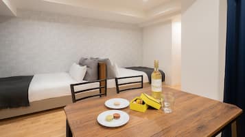 A hotel room with a bed, a wooden table with a bottle and glasses, and a box of macarons.