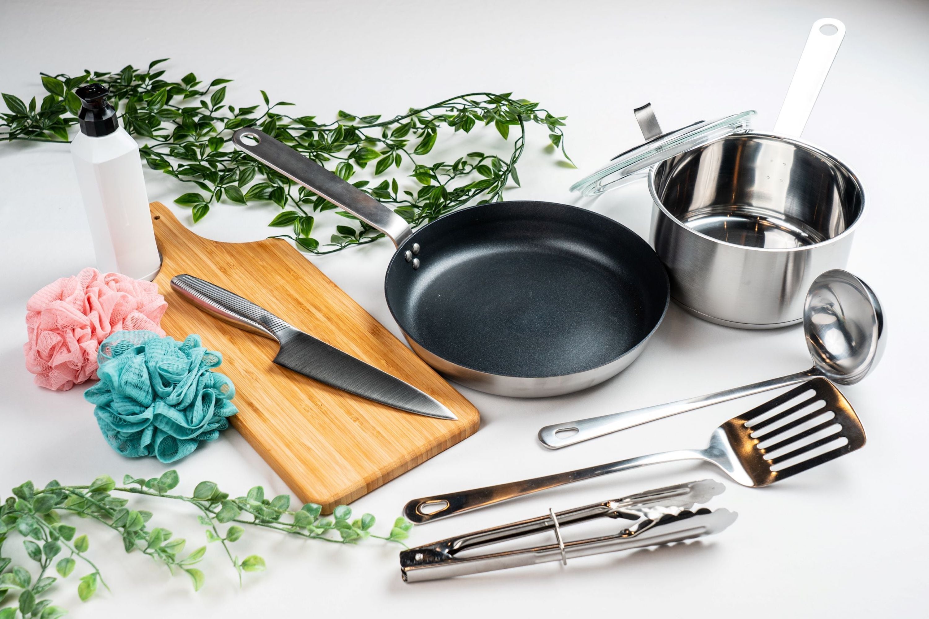 A kitchen setup with a wooden cutting board, a knife, a frying pan, a pot, a strainer, and kitchen utensils.