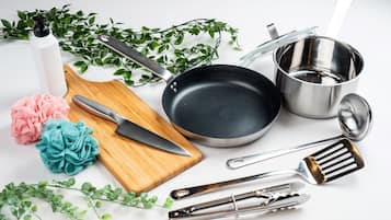 A kitchen setup with a wooden cutting board, a knife, a frying pan, a pot, a strainer, and kitchen utensils.