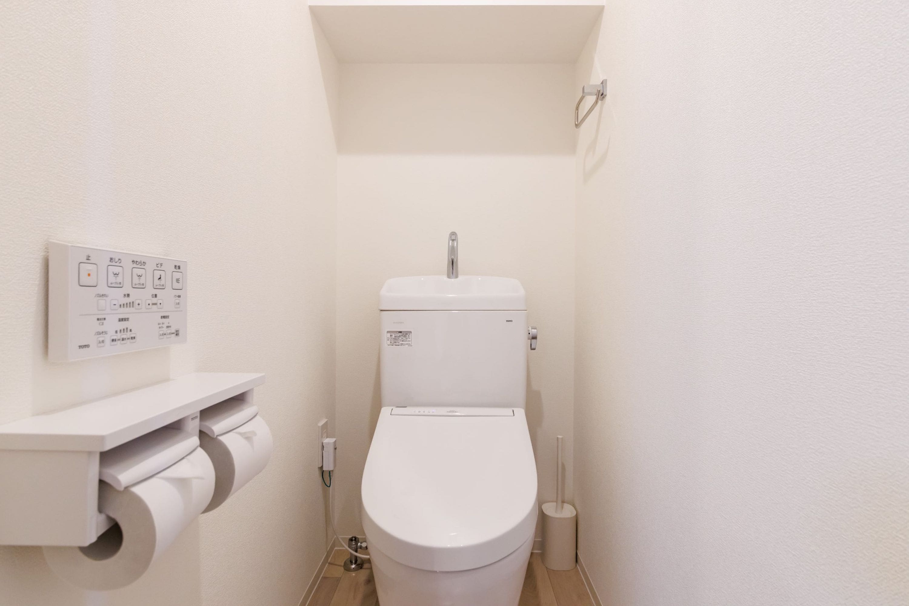A small, white bathroom with a toilet, a toilet paper holder, and a hand dryer.