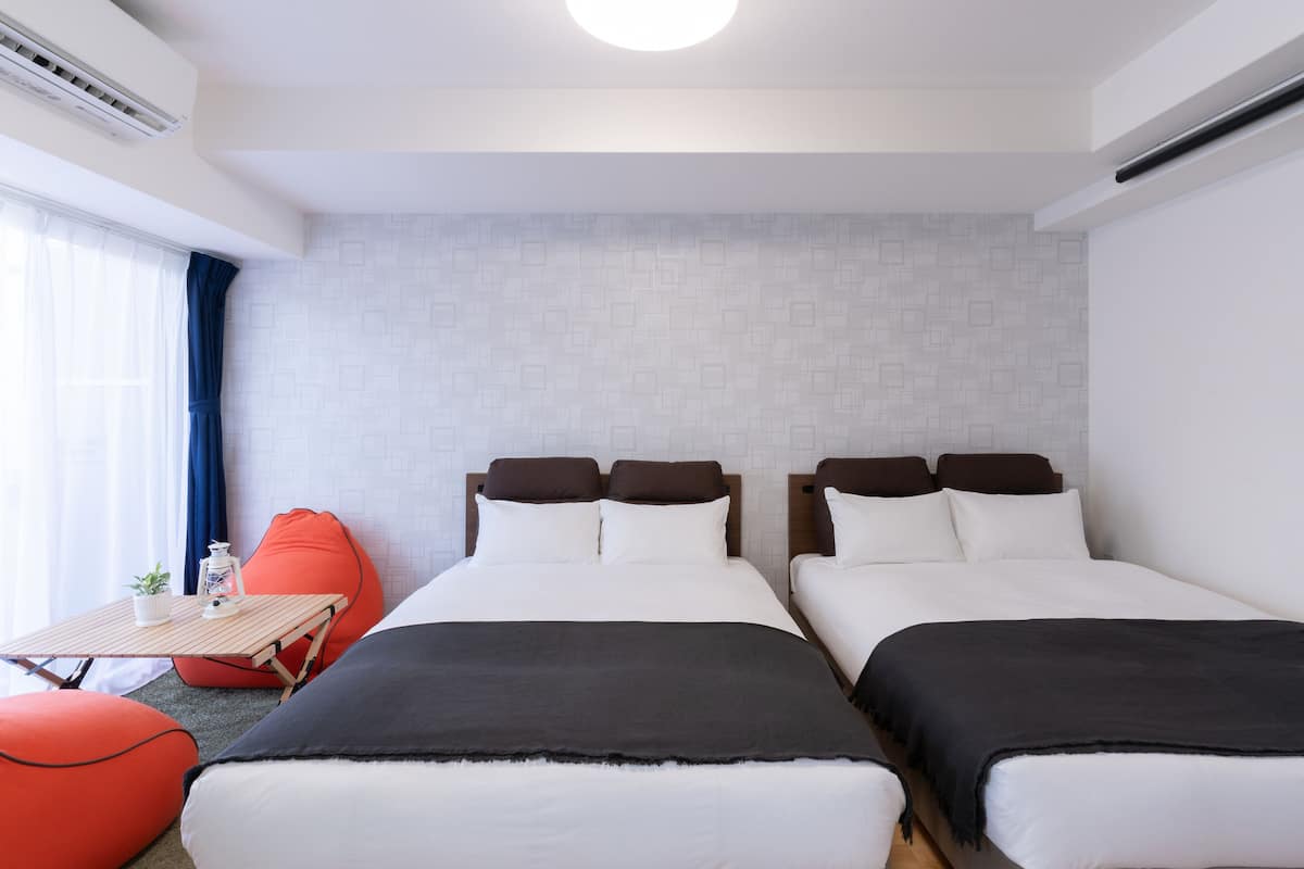 Een hotelkamer met twee éénpersoonsbedden, een kleintje tafeltje met een plant en een rode relaxfauteuil.