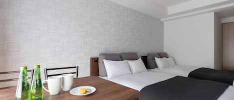A hotel room with a bed, a wooden table with two bottles and a mug, and a plate with a lemon.