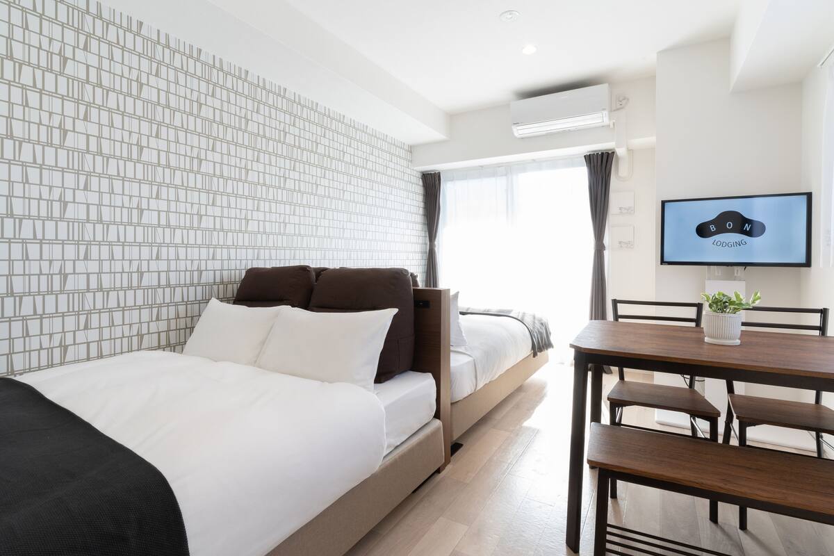 Een moderne hotelkamer met een bed, een bureau en een televisie waarop 'BON LODGING' staat.