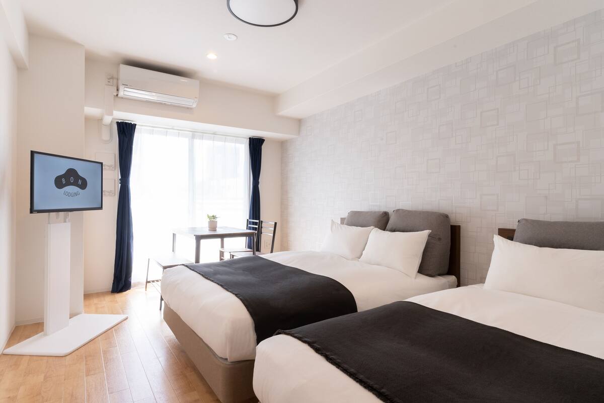 Hotelkamer met twee bedden, een televisie, een airconditioner en een raam met gordijnen.