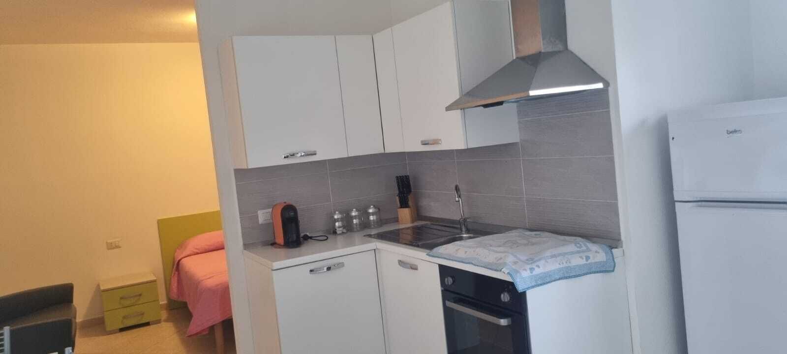 A compact kitchen with white cabinets, a stainless steel range hood, a sink, and a refrigerator.