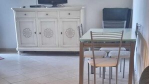A living room with a sofa, a dining table with chairs, a cabinet, and a television. - Piccolo Apartment for 2 people (Budoni)