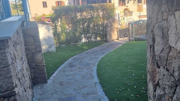 A stone pathway leading to a green lawn area, flanked by stone walls and a hedge. - Piccolo Apartment for 2 people (Budoni)