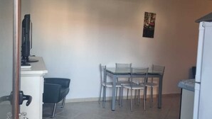 A small dining area with a table and four chairs, a television on a stand, and a refrigerator. - Piccolo Apartment for 2 people (Budoni)