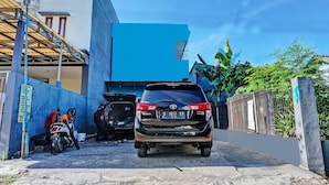 A black SUV parked in a narrow driveway with a blue building in the background. - OYO Life 91718 Kost Damai Syariah (Sidoarjo)