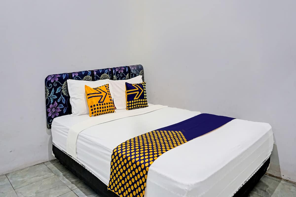 Una cama con colchón blanco, cabecera estampada en azul y amarillo, y dos almohadas con diseños geométricos.