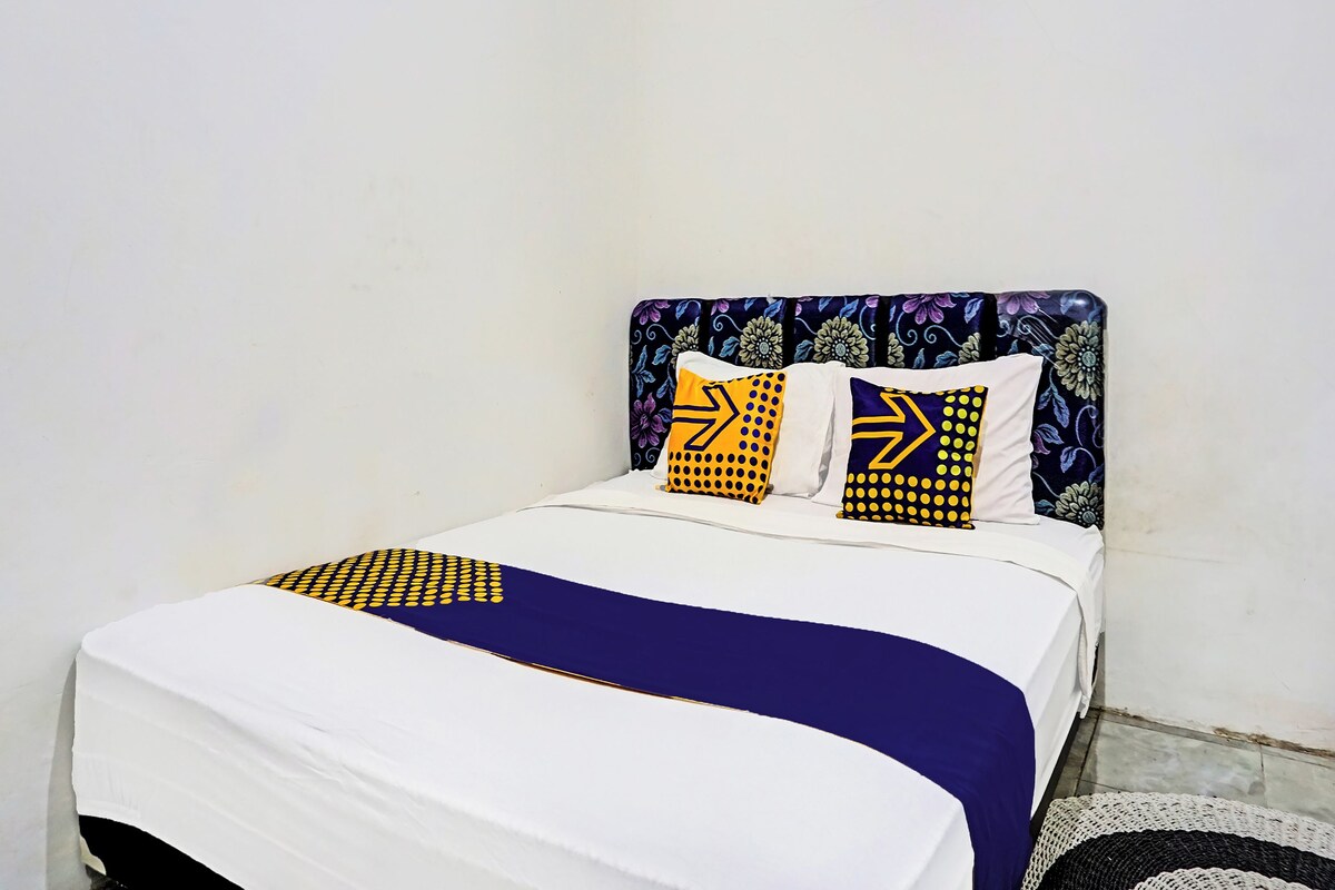Ein Bett mit einer weißen und blauen Tagesdecke, zwei Kissen mit gelb-blauen Mustern und ein Kopfstück mit floralem Dekor.