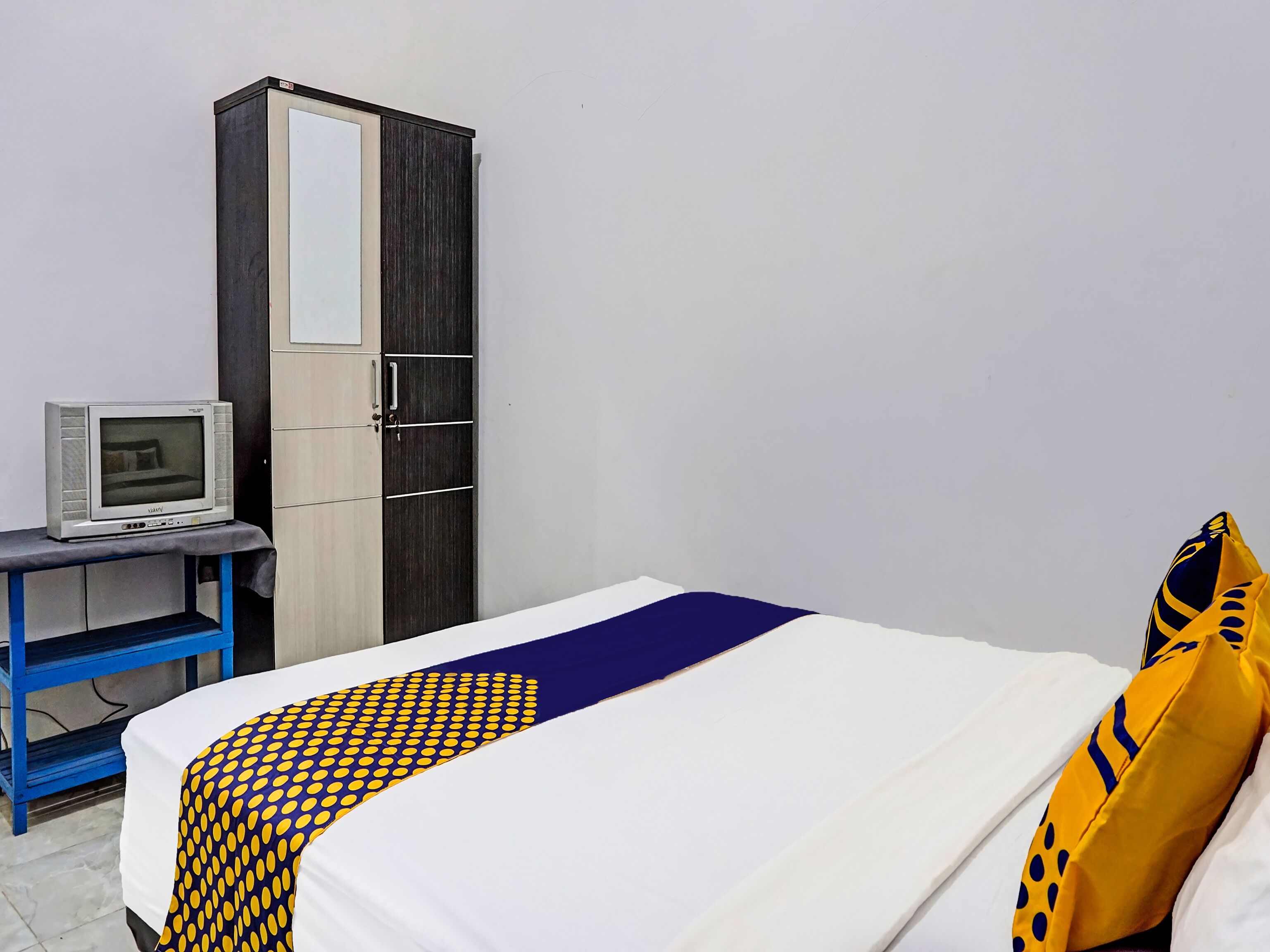 A bedroom with a bed, a wardrobe, a desk with a computer, and a patterned blanket.