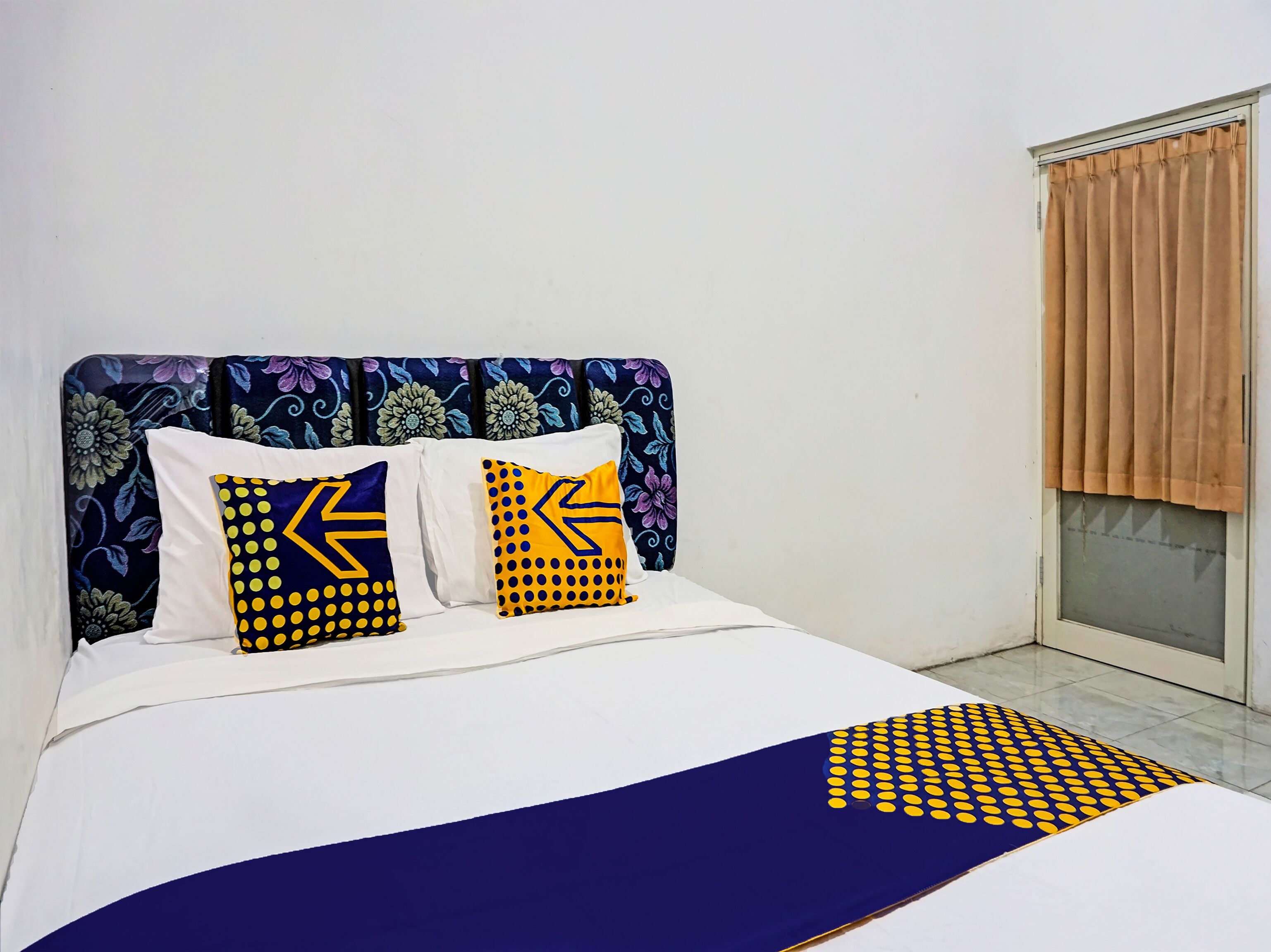 A bed with a patterned headboard, two pillows with geometric designs, and a blue and yellow bedspread.
