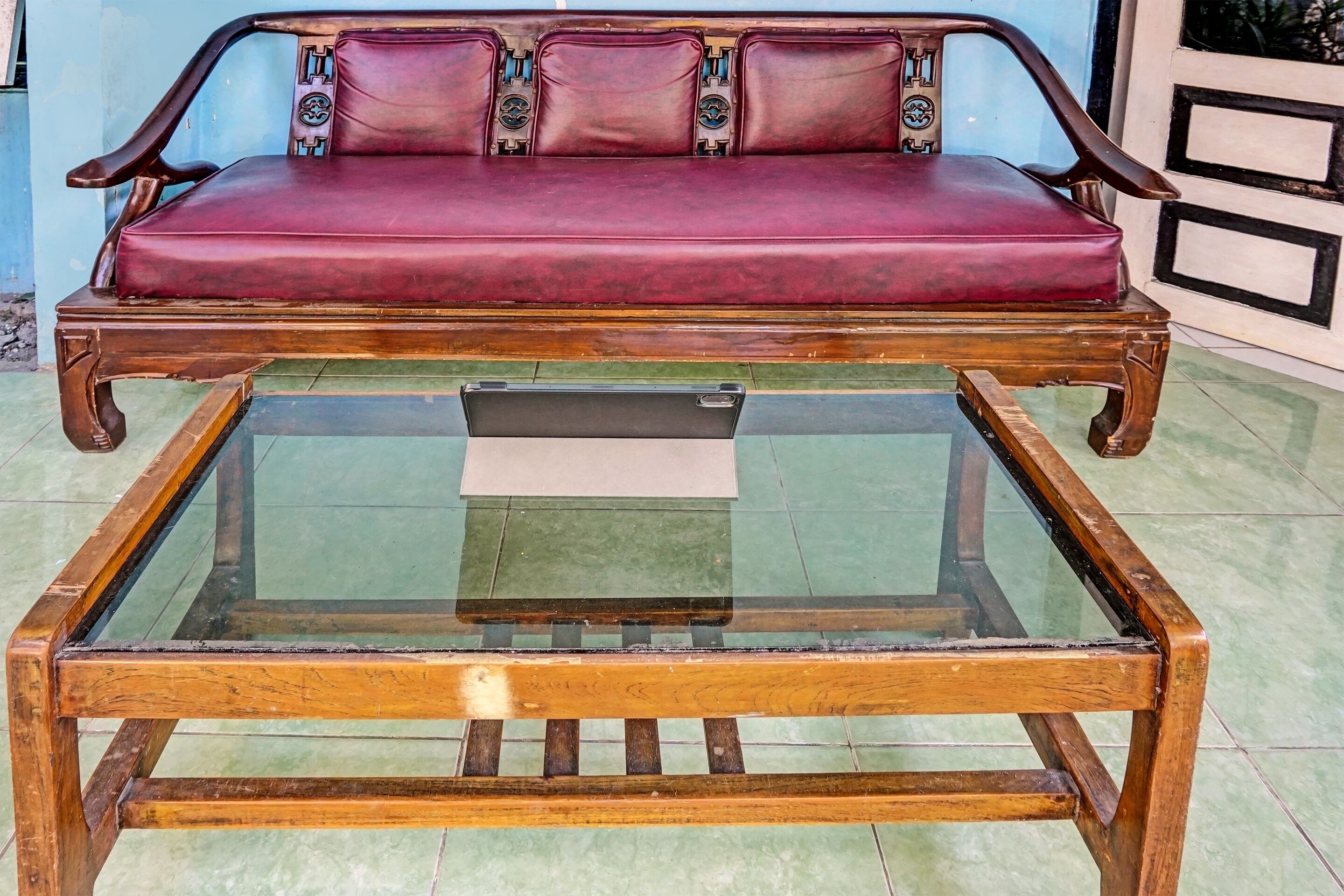 Ein Holzsofa mit roten Kissen und einem Glastisch.