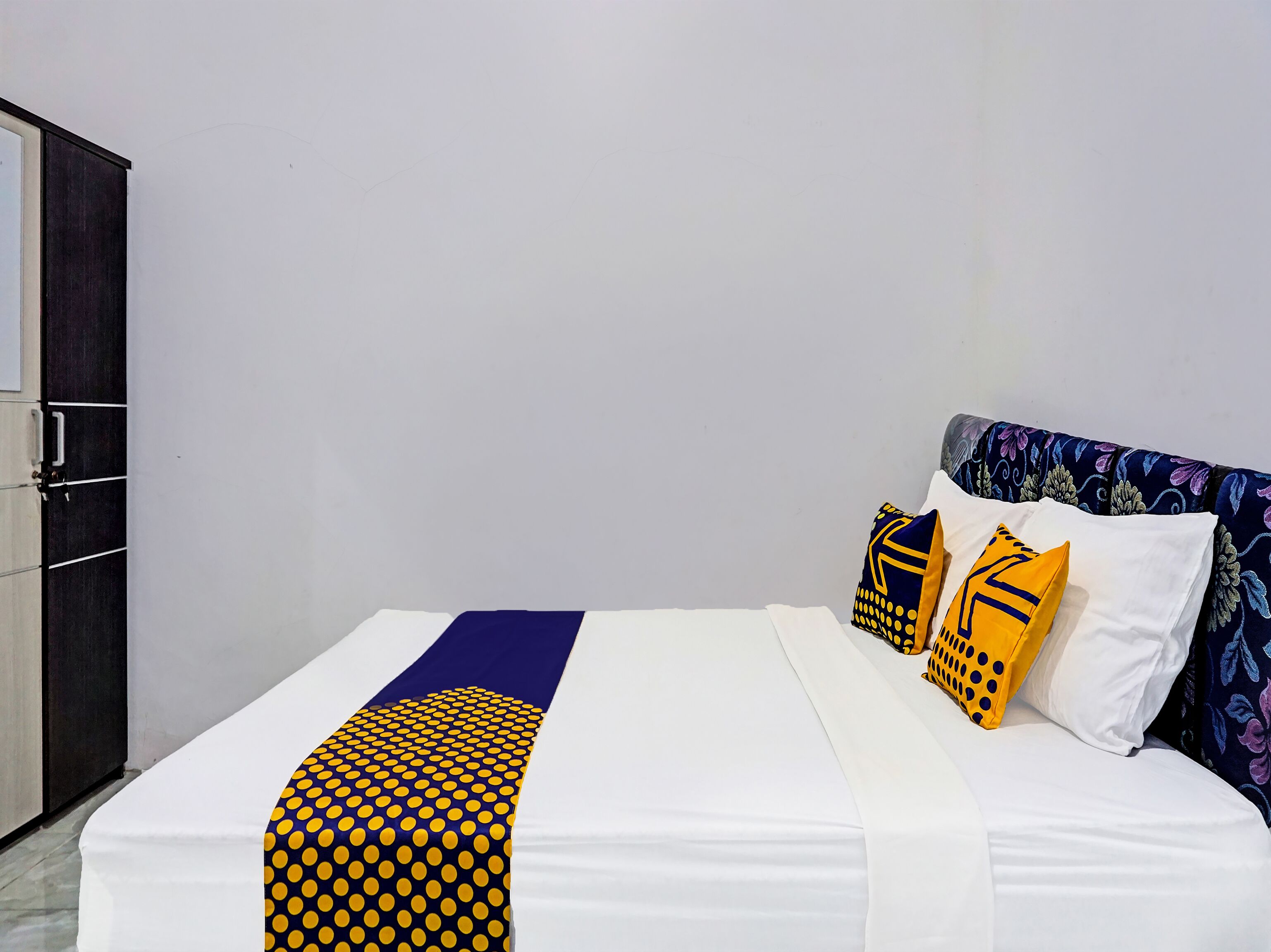 Ein Bett mit weißer Matratze, einer Decke in Blau und Gelb gebändert und zwei Kissen mit gelb-blauen Mustern.