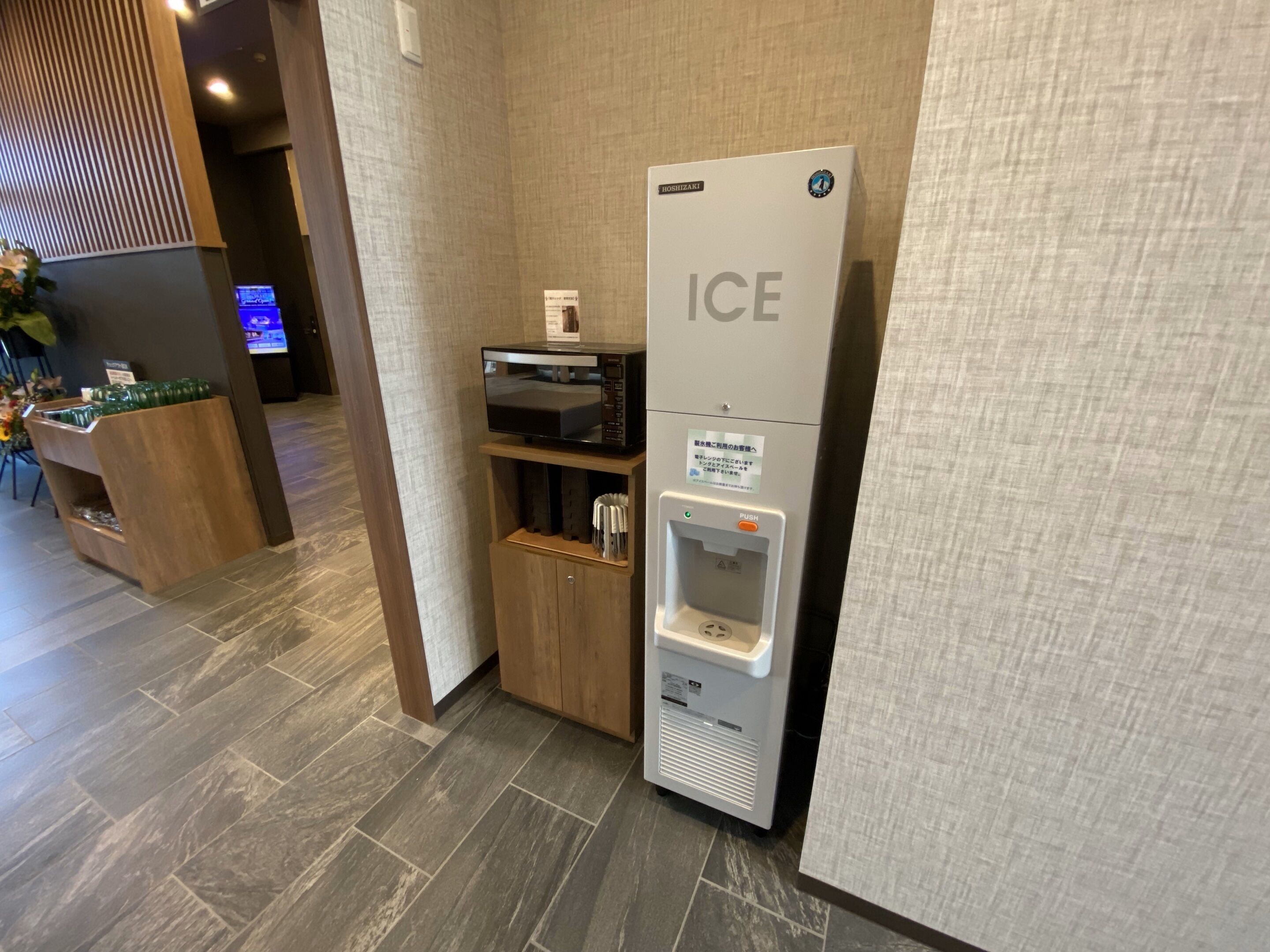 A hotel reception area with a modern design, including a reception desk, a digital screen, and a self-service ice dispenser.
