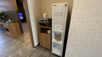 A hotel reception area with a modern design, including a reception desk, a digital screen, and a self-service ice dispenser.
