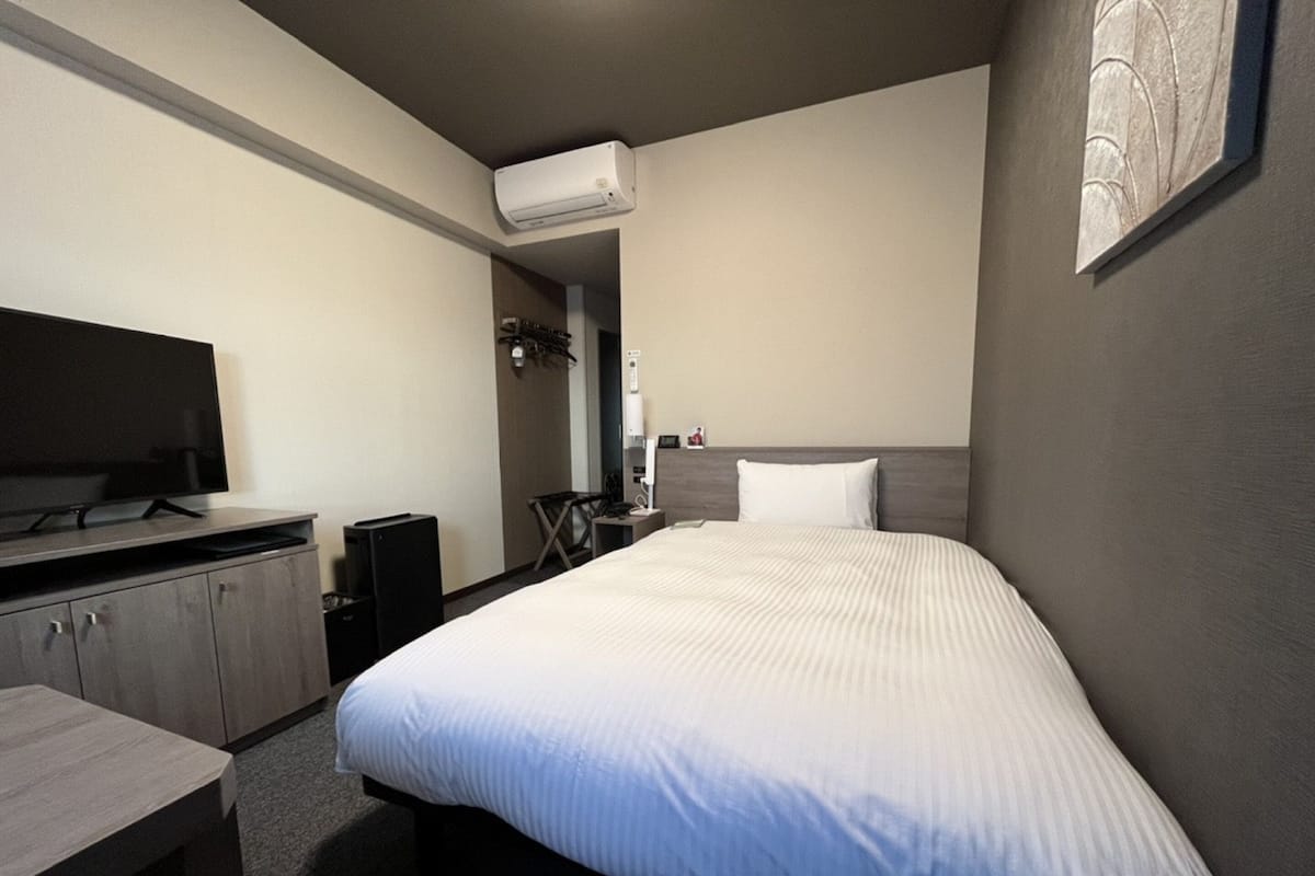 A hotel room with a bed, a desk, a TV, and an air conditioning unit.