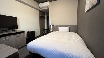 A hotel room with a bed, a desk, a TV, and an air conditioning unit.