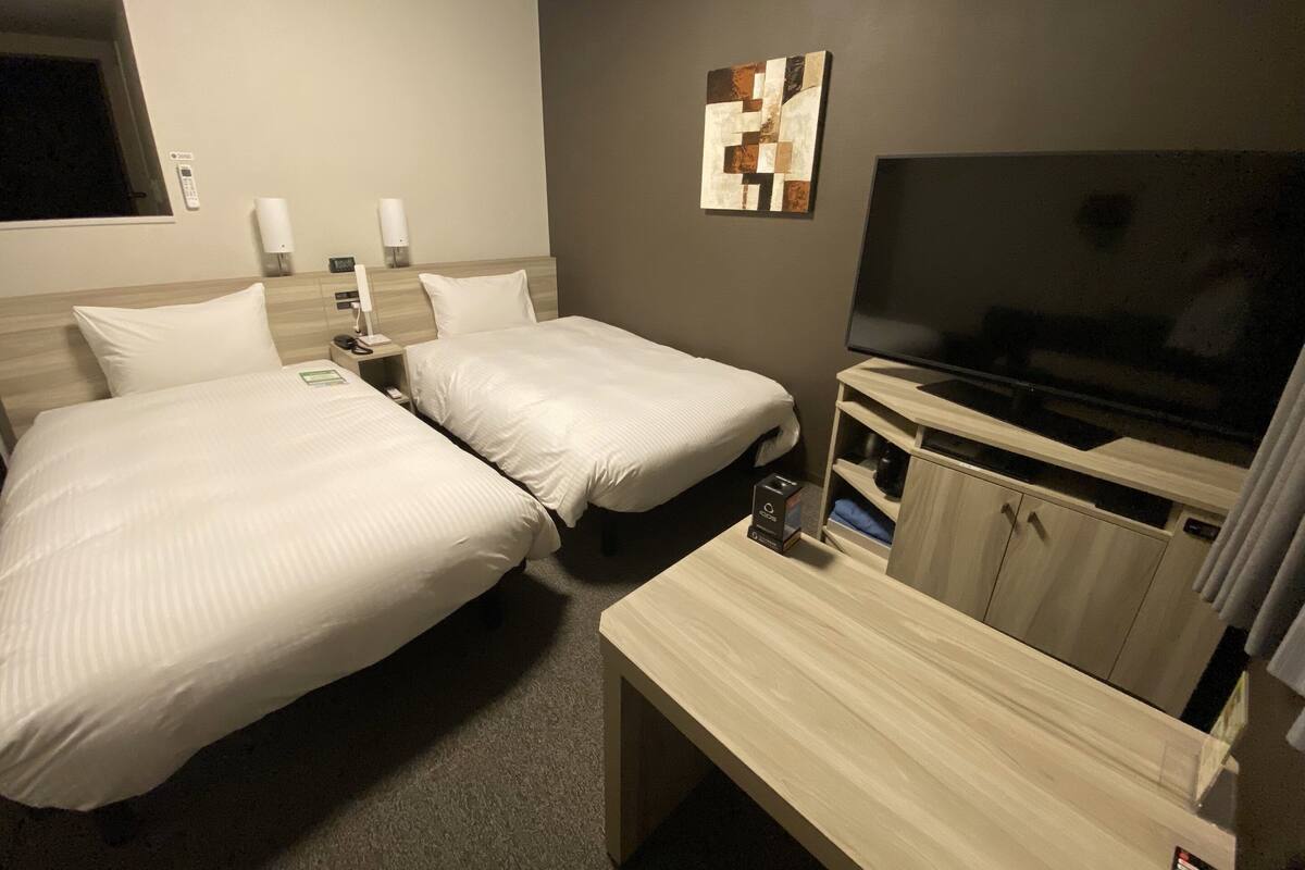 A hotel room with two beds, a TV, a desk, and a cabinet.
