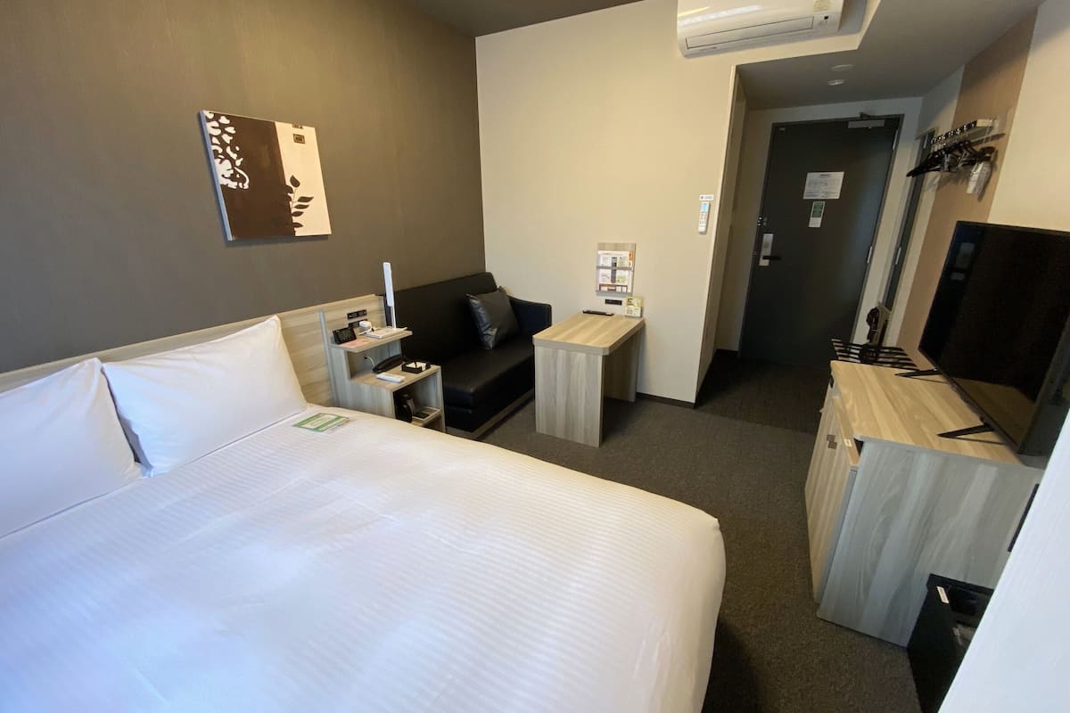 A hotel room with a bed, a desk, a sofa, and a television.