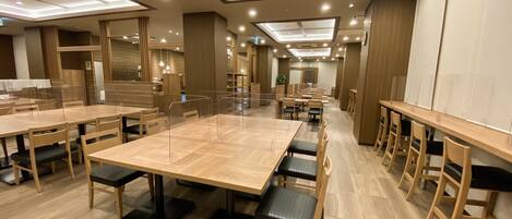A spacious dining area with multiple tables and chairs, wooden flooring, and recessed ceiling lighting.