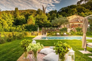 A private pool area with a stone house, lush greenery, and a wooden deck with outdoor seating. - Villa Ester, a Stylish Farmhouse with Pool on the Hills by Lucca (Capannori)