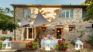 A stone house with a patio set up for dining, featuring a table with white tableware and potted plants. - Villa Ester, a Stylish Farmhouse with Pool on the Hills by Lucca (Capannori)