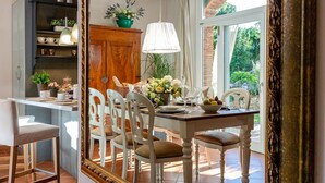 A dining area with a table set for four, surrounded by white chairs, a wooden cabinet with kitchenware, and a large mirror reflecting the room. - Villa Ester, a Stylish Farmhouse with Pool on the Hills by Lucca (Capannori)