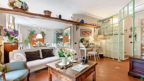 A cozy living room with a sofa, coffee table, and decorative items. There is a dining area with chairs and a table, and a kitchen in the background. - Villa Ester, a Stylish Farmhouse with Pool on the Hills by Lucca (Capannori)