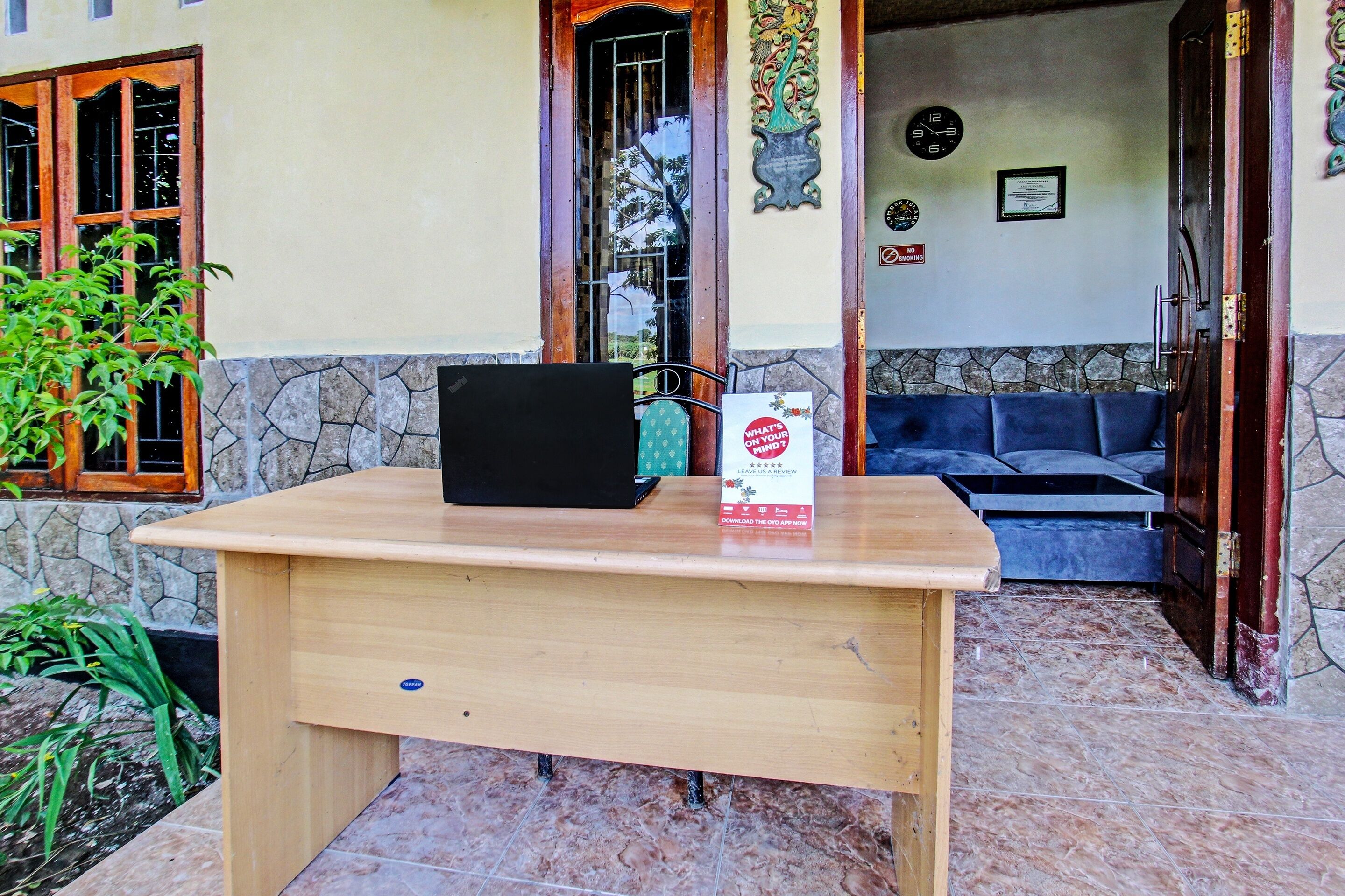 Een houten bureau met een laptop en een bordje voor een gebouw met een stenen muur en een blauwe bank.