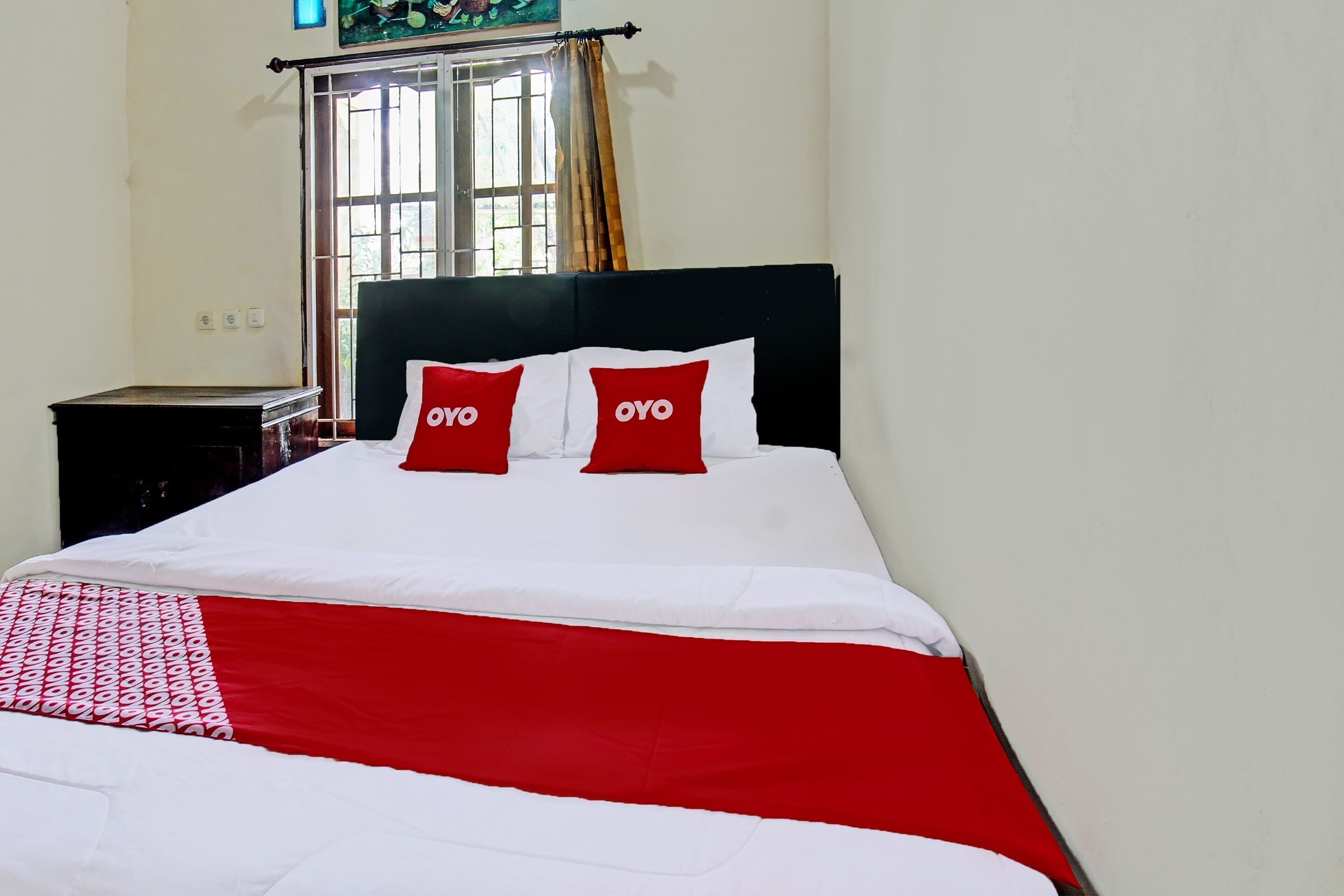 A neatly made bed with a black headboard and two red pillows with "OYO" branding.