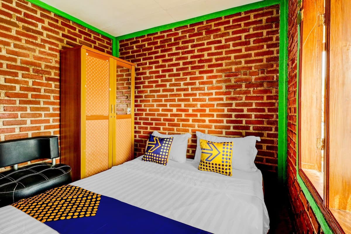 A room with a brick wall, a bed with patterned pillows, a black headboard, and a wooden door.